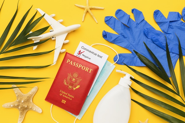 色付きの背景にコロナウイルステスト結果マスクおよびその他の衛生製品を備えたアメリカのパスポートを使用したフラットレイ組成