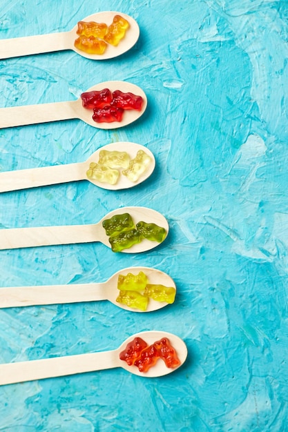 Flat lay composition with delicious jelly bears candy in wooden spoon gummy bear on blue background top view copy space