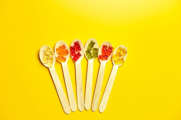 Flat lay composition with delicious jelly bears candy in wooden spoon gummy bear on yellow background top view copy space