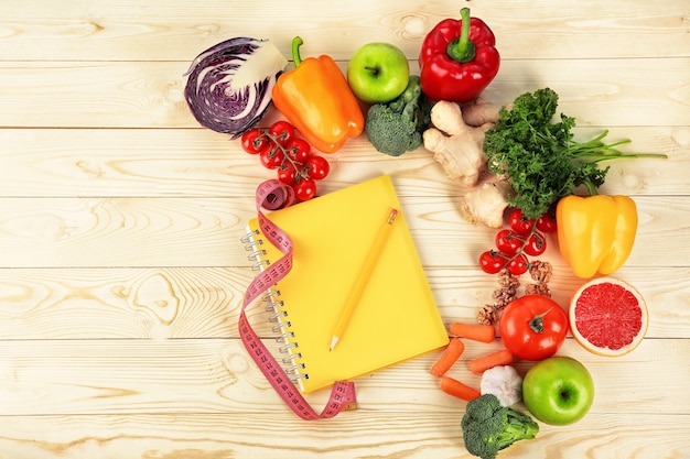 Flat lay composition with diet food, notebook and measuring tape on wooden wall