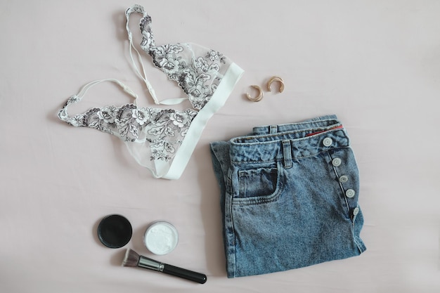 Flat lay composition with female underwear bra jeans cosmetics and accessories on beige background