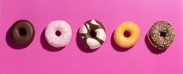 Flat lay composition with mixed donuts on  pink background.