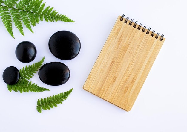 Flat lay composition with spa stones green ferns and a notebook with space for text Relaxation spa treatment concept