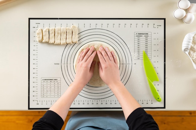 Flat lay of cook hands kneading rolled out dough on a silicone baking mat with round markings of different diameters