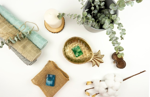 A flat lay of cotton towels, hand made soap, a pot with eucalyptus and a branch of cotton on a white table in a modern bathroom