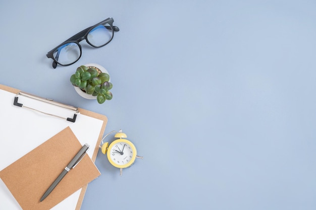 Flat lay craft notepad pen yellow alarm clock and eyeglass on a blue background business women concept Top view and copy space