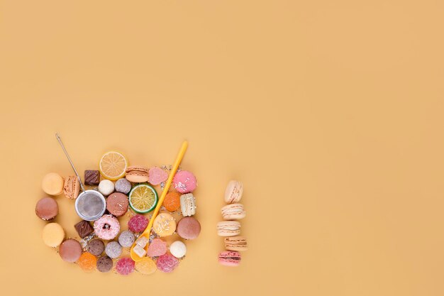 Flat lay of a cup of tea consisting of macaroons donuts lemons tea strainer on yellow background