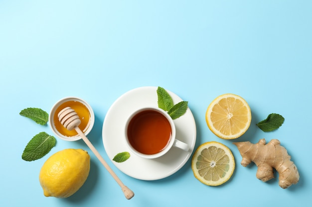 Flat lay. Cup of tea, lemon, ginger, mint, honey and dipper on blue, copy space