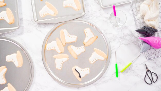 Flat lay. Decorating ice skate shaped sugar cookies with black color royal icing.