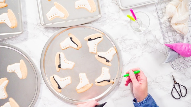 Flat lay. Decorating ice skate shaped sugar cookies with black color royal icing.