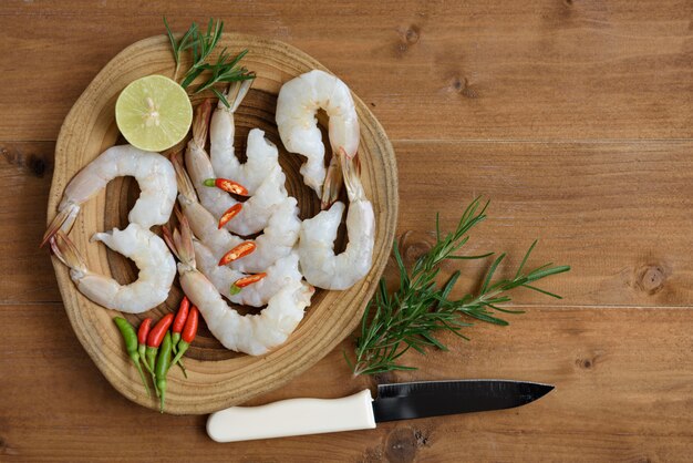 Foto design piatto laici, gamberetti crudi, lime, peperoncino e sedano, pomodoro e rosmarino impostato su vassoio di legno su ingrediente piccante tailandese di legno