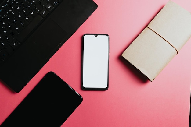 Flat lay design of a working space over pink pastel background. Mobile phone with blank space, copy space to fill with a image. Minimal and colorful space work. Laptop tablet netbook and computer