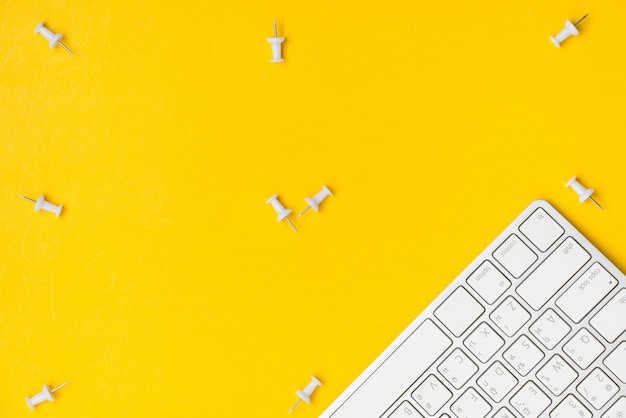 Flat lay of desktop workspace white push pin and keyboard with blank space on yellow background