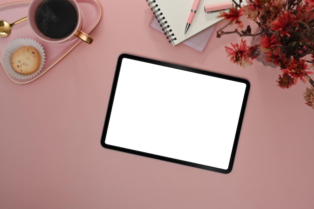 Flat lay digital tablet with blank screen coffee cup and notebook on pink background