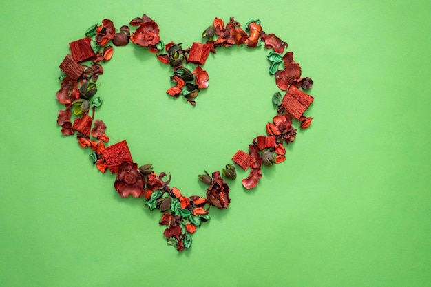 Flat lay dry petals in the form of a heart with a place for text on an green background copy space