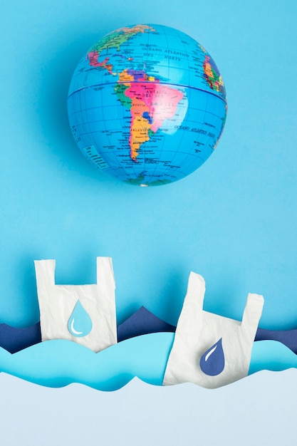 Flat lay of earth globe with paper ocean waves and plastic bags