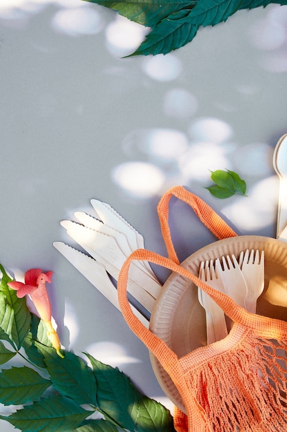 Flat lay of eco craft paper and wooden tableware, summer sunlight, Zero waste, plastic-free and eco-friendly living, paper cups, dishes, bag, plates and wooden cutlery in cotton mesh bag.