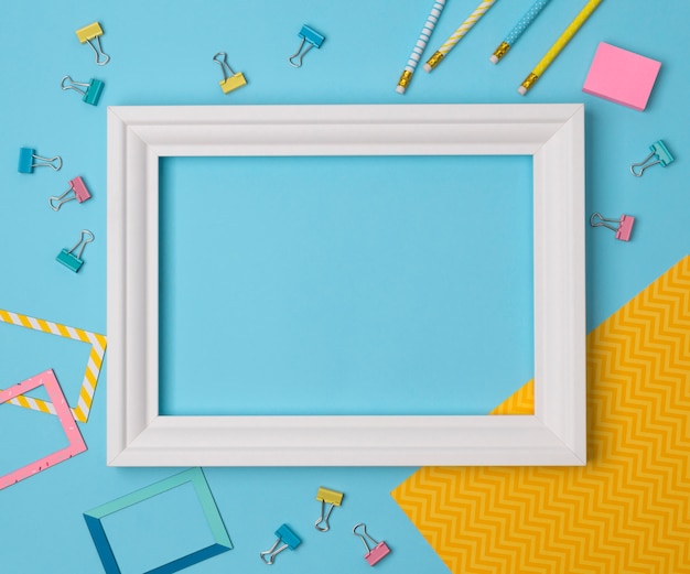 Flat lay empty frame and office supplies on blue pastel table