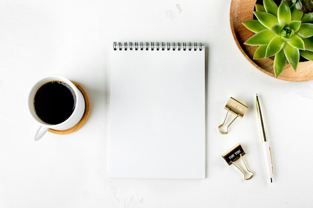 Flat lay fashion home office workspace with succulent, cup of coffee, blank paper notebook, pen and clips. Top view. copy space.