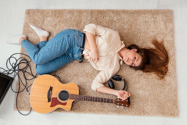 Flat lay of female musician on the floor at home with headphones and acoustic guitar