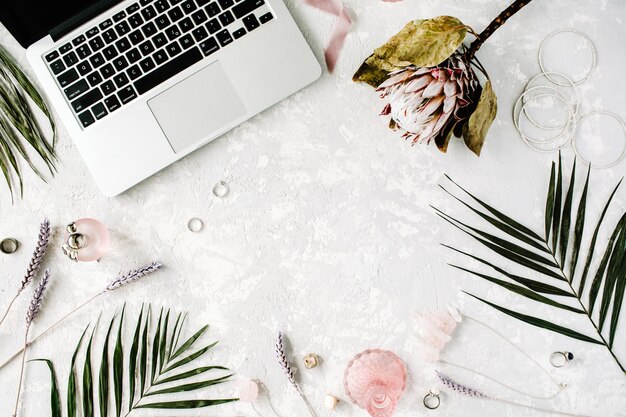 Flat lay feminine home office workspace with laptop, proteus
flower, necklace, palm branches and accessories