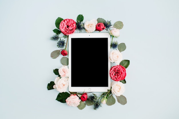 Плоская цветочная рамка с таблеткой, бутонами красных и бежевых роз на бледно-пастельно-синем фоне. Вид сверху