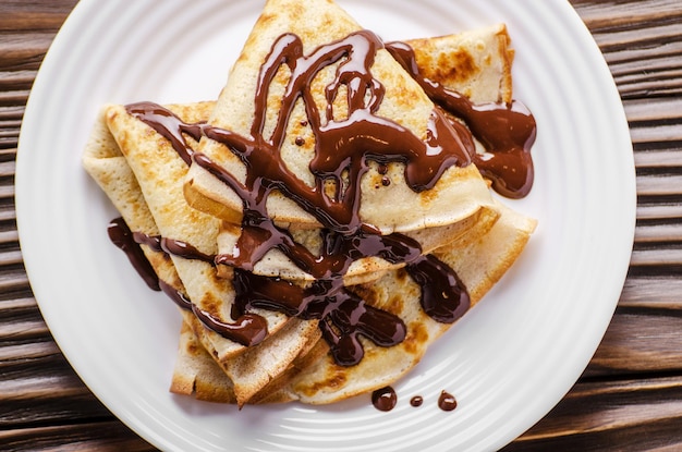 Flat lay French crepes with chocolate sauce in ceramic dish on wooden kitchen table