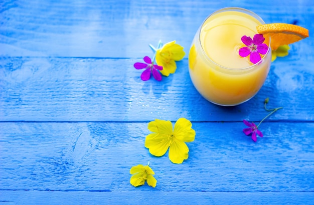 Flat lay of fresh orange juice garnished with a slice of ripe orange and flowers on the blue wooden table