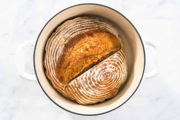 Disposizione piatta pagnotta appena sfornata di pane a lievitazione naturale di grano con segni di cestello per lievitazione del pane in ghisa smaltata forno olandese