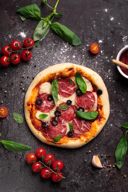 Flat lay of freshly baked pizza with olives and basil and ingredients on a black background