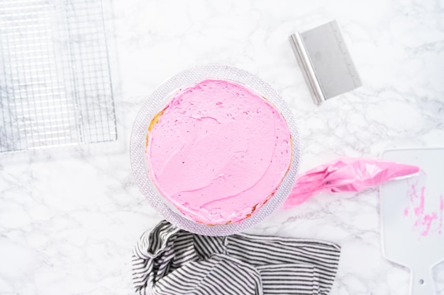 Flat lay. Frosting a tall round cake with pink buttercream icing.