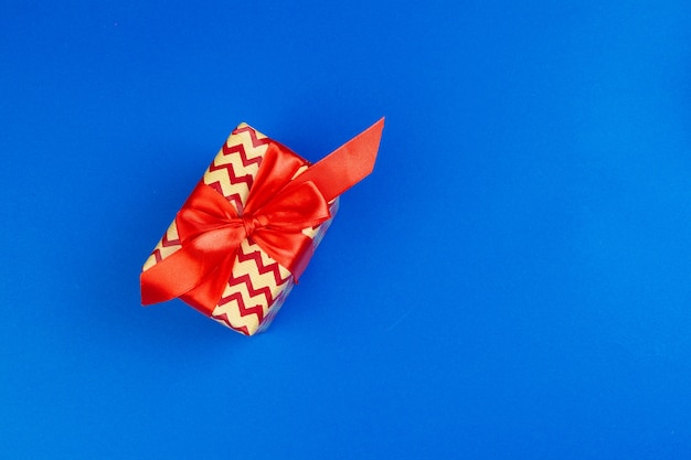 Flat lay of gift box decorated with bow on blue background