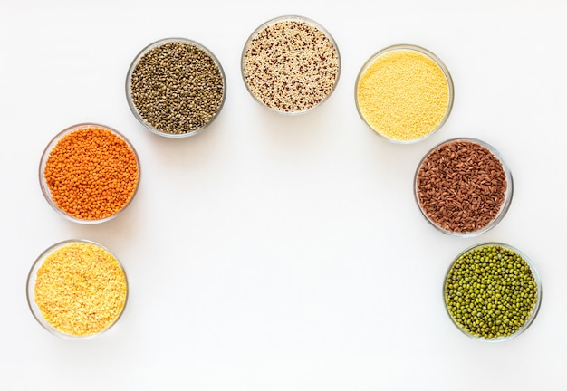 Flat lay glass bowls with superfoods are standing as arc on white background with copy space in middle.