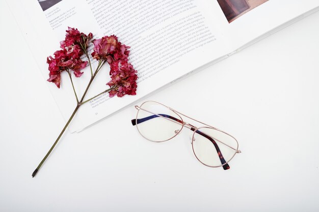 Posare gli occhiali per vedere un libro e fiori appassiti con uno spazio bianco