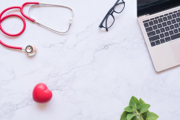 flat lay of good healthy concept red heart and stethoscope and laptop on white marble background