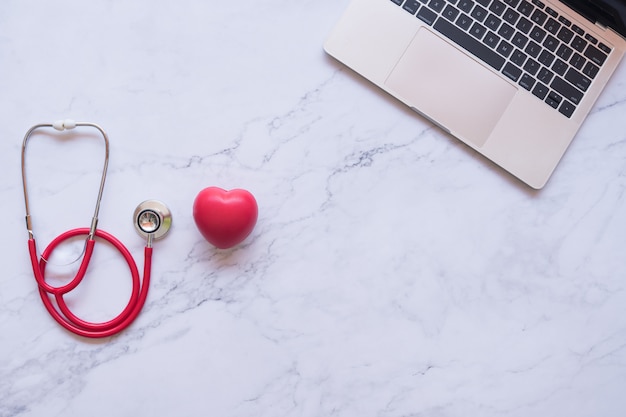 Flat lay of good healthy concept,  red heart and stethoscope and laptop on white marble background 