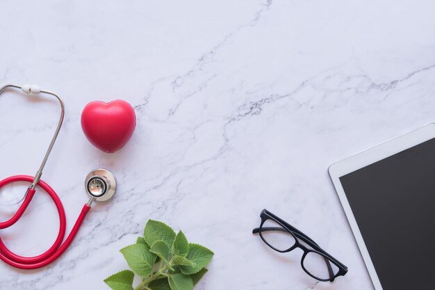 flat lay of good healthy concept red heart and stethoscope and tablet on white marble background