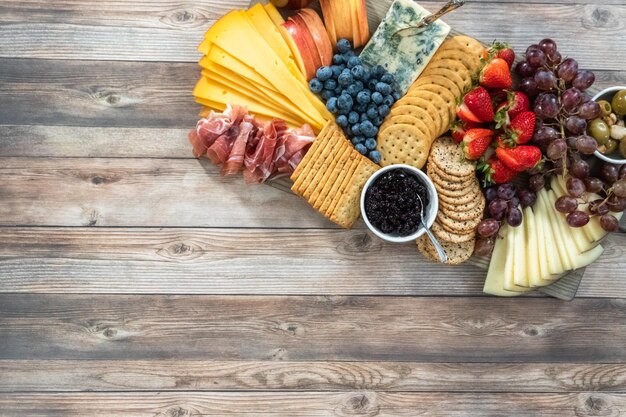 Flat lay. Gourmet cheese, crackers, and fruit on a wood cutting board served as an appetizer.