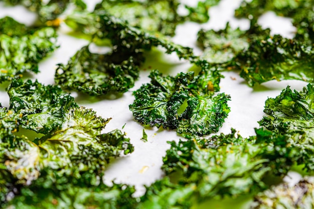 Flat lay of green kale chips with salt on white background. Healthy vegan food concept.