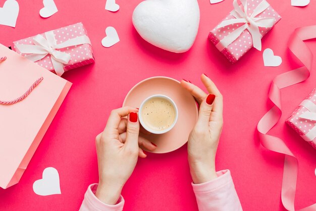 Flat lay of heart shaped cup of black coffee in the hands of women on colored background with copy space top view Valentine day and holiday concept