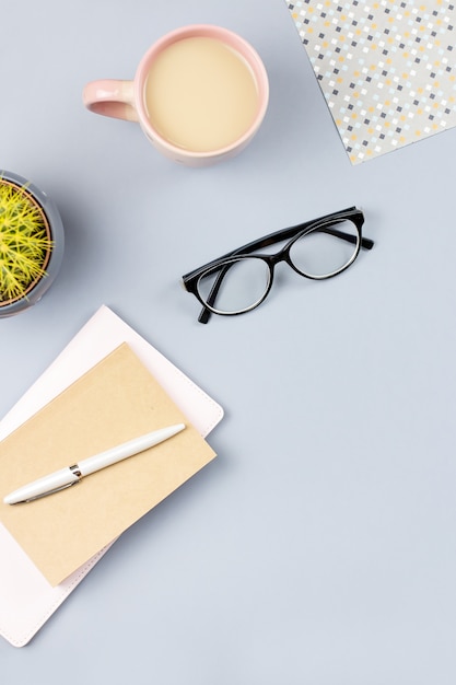 Flat lay home office desk. Female workspace with note book, eyeglasses, tea mug, diary, plant. Copy space