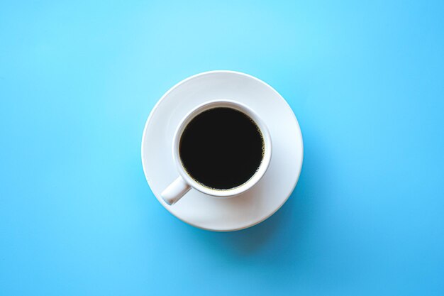 Flat lay of hot americano coffee in white coffee cup on blue background