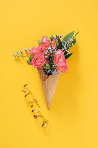 Photo flat lay ice cream cone with colorful bouquet on yellow, copy space