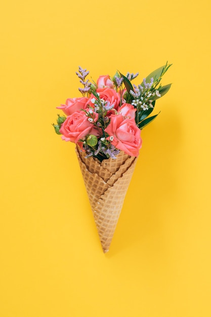 Photo flat lay ice cream cones with colorful bouquet on yellow, copy space