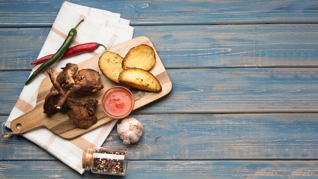 Costolette di agnello distese su tavola di legno con patate e salsa con copia-spazio