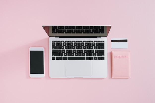 Flat lay of laptop, credit card, mobile phone and passport on pink background