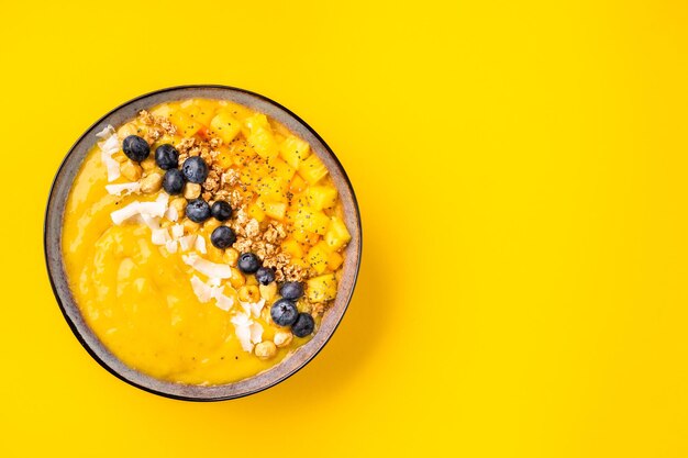 Flat lay of mango smoothie bowl on yellow background copy space