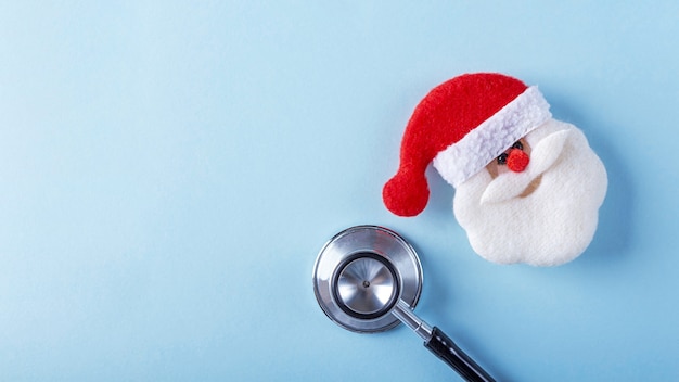 Flat lay medical Christmas composition with stethoscope and Santa Claus toy on blue