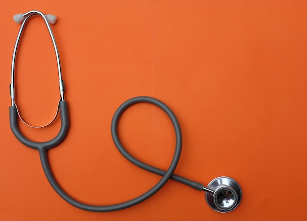 Photo flat lay medical stethoscope on orange background in doctors desk