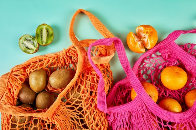 Flat lay Mesh grocery shopping eco friendly bag with kiwi and tangerine fruits on green canvas background Zero waste cconcept Local farmers market shopping mall top view copy space Plastic free items